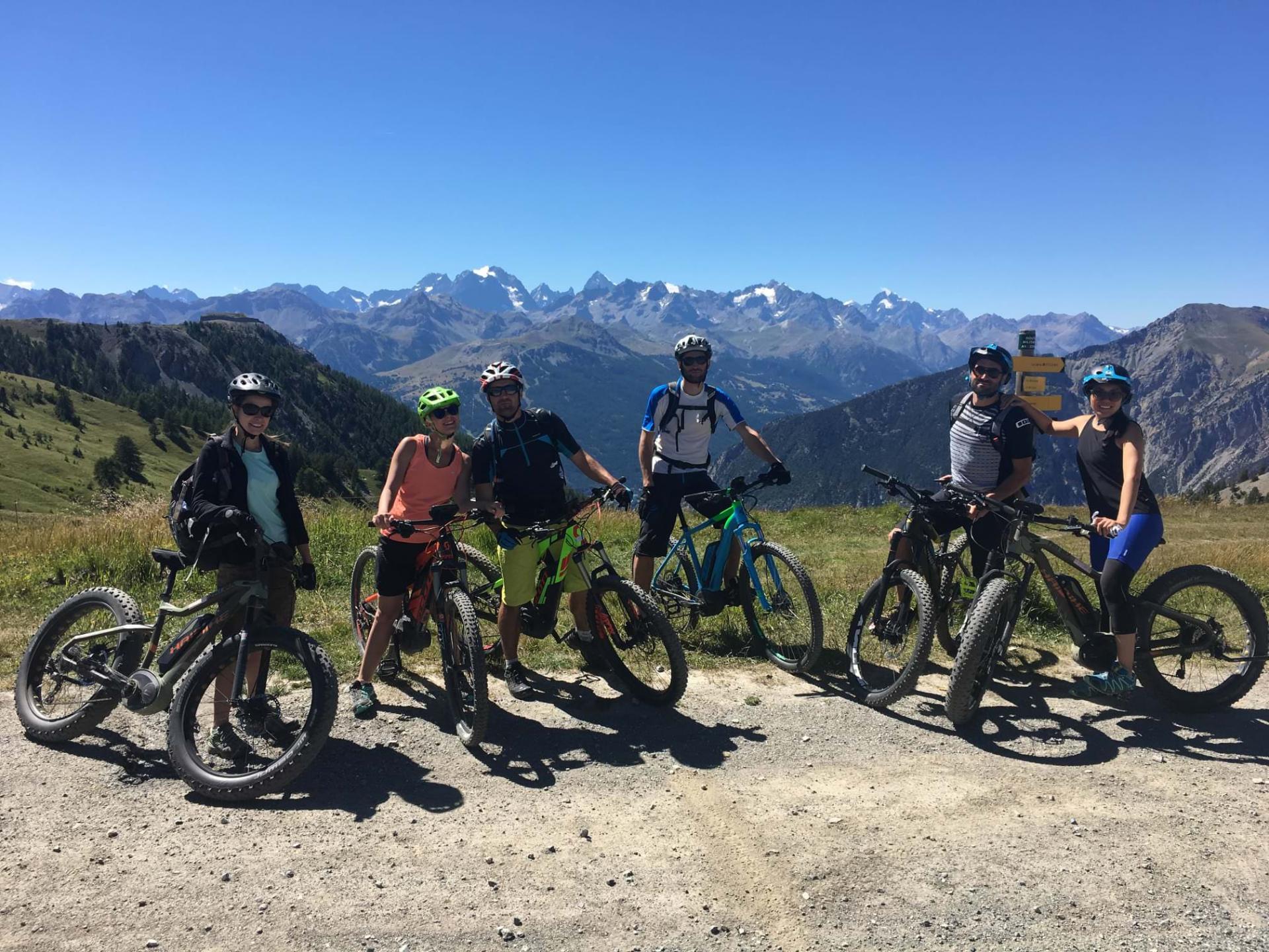 A small group of riders pausing on a high alpine col, the Écrins peaks behind them